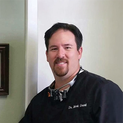 Dentist Mark Grant Smiling In Front Of White Wall